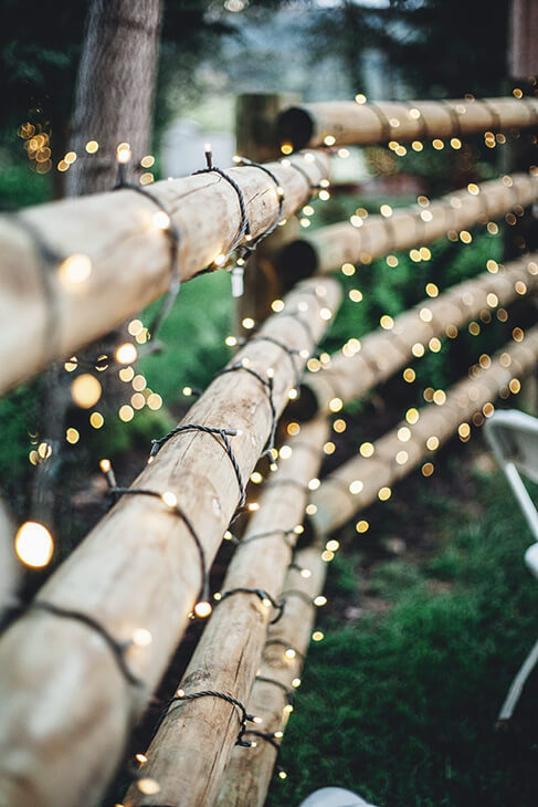 log fencing covered with christmas lights in a forest