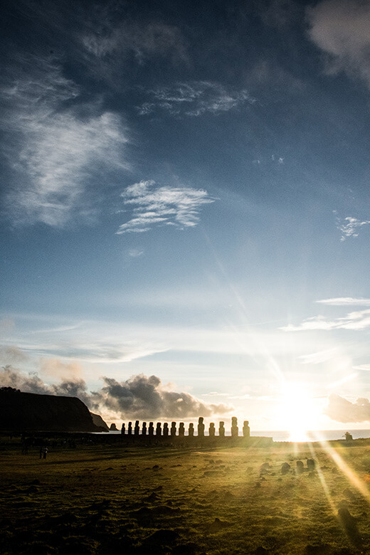 a sunrise on easter island with the light coming through the Moai statues