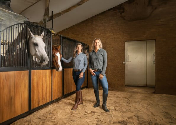 AI image of women standing in front of horse stalls.