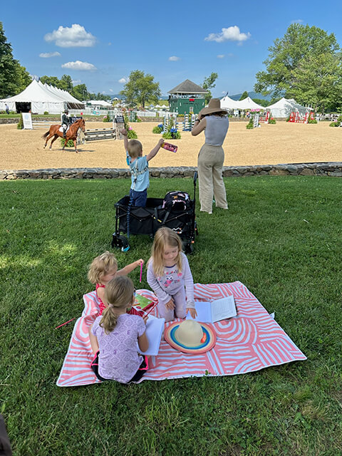 kids on a picnic blanket with a photographer photographing a horse at upperville horse show in the background